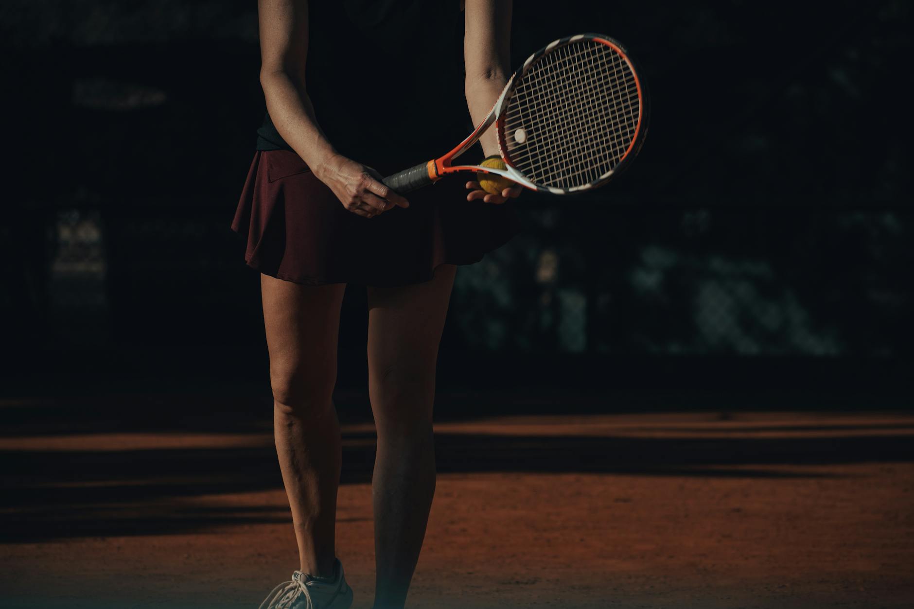 Female tennis player ready to serve on a clay court, holding a racket and tennis ball.