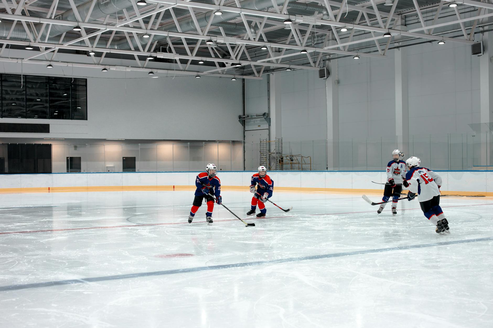 Young athletes playing ice hockey in a spacious indoor arena, showcasing teamwork.
