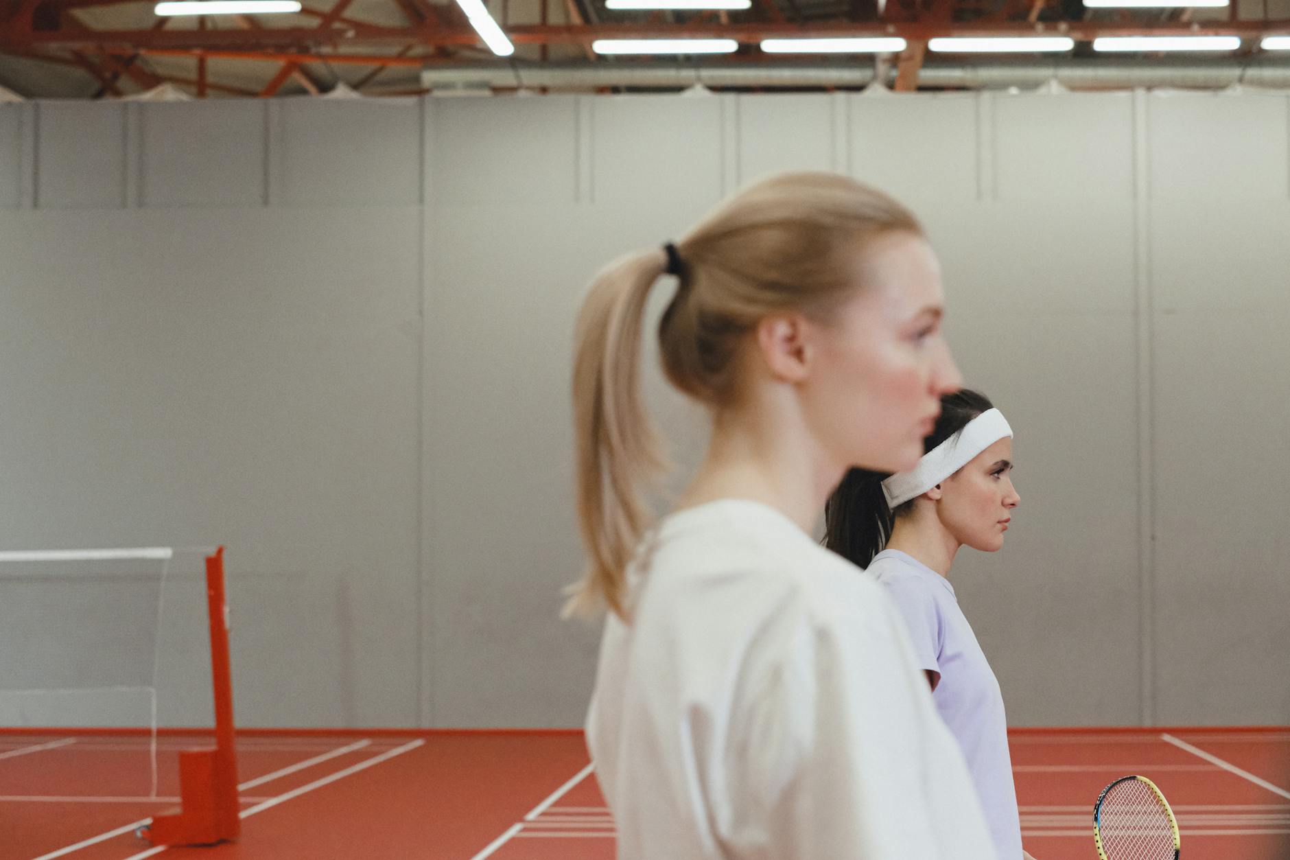 Two women playing tennis indoors with focus on their profiles. Ready for the game.