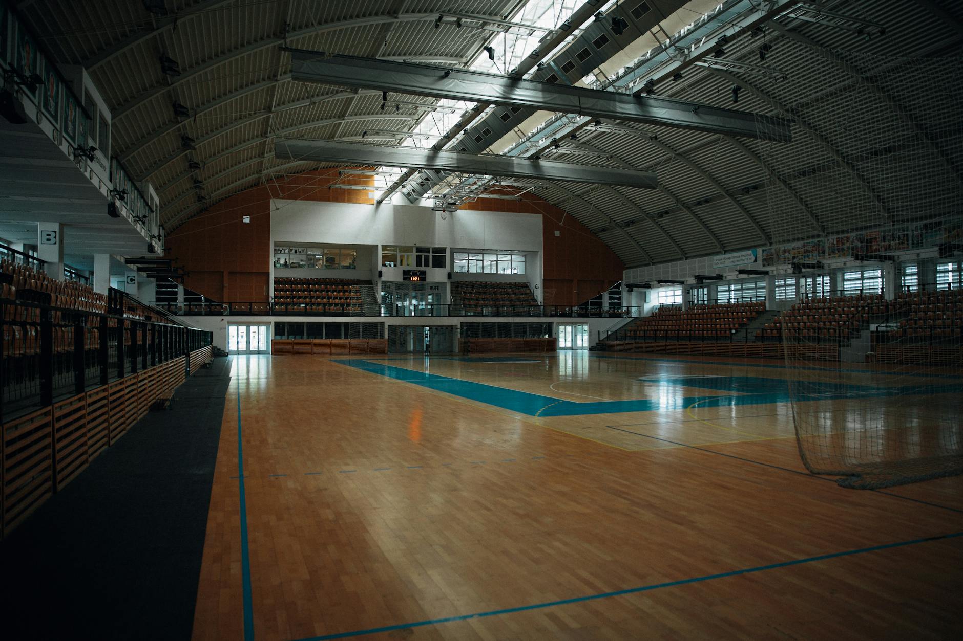Empty indoor sports arena with hardwood flooring and bleachers, perfect for various sports activities.