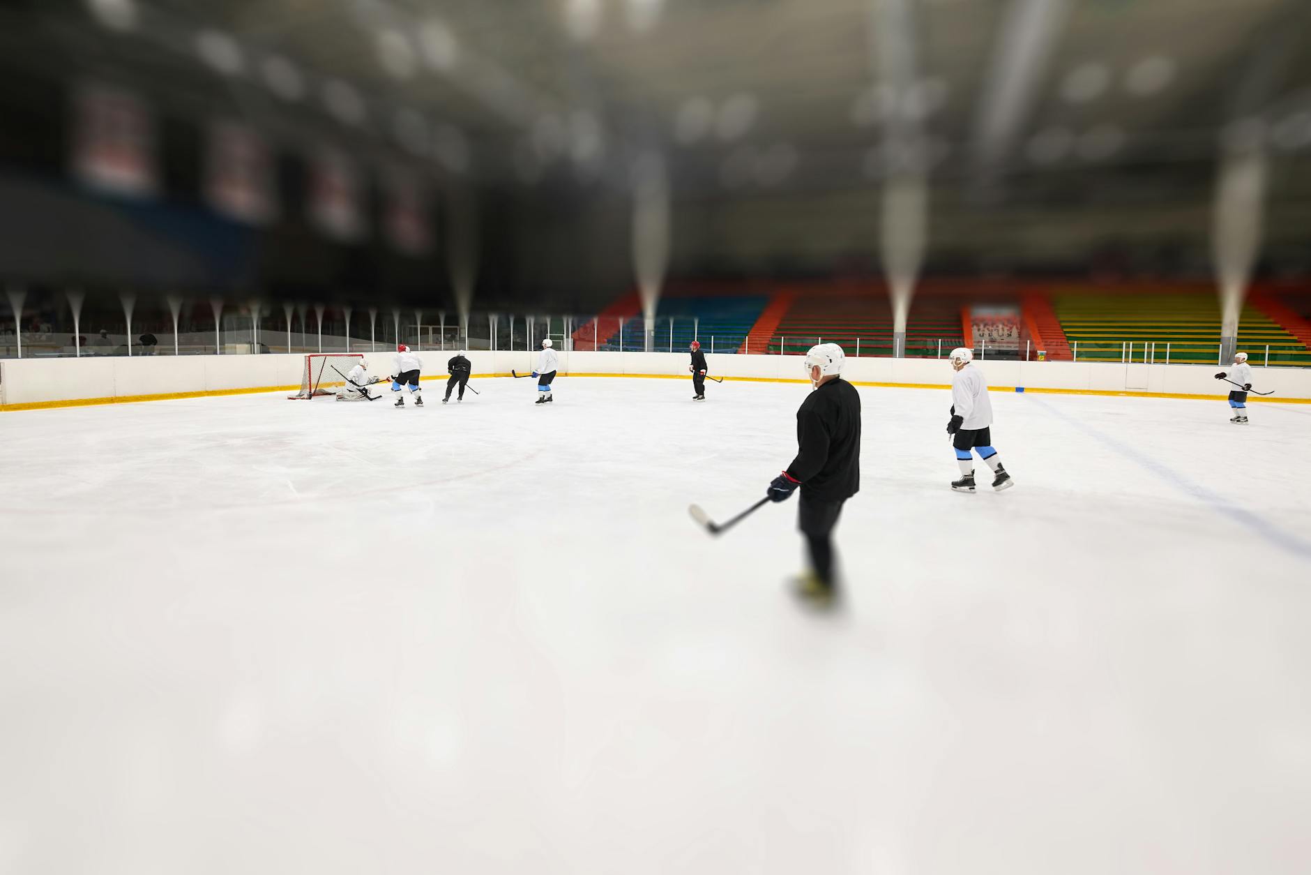 A group of hockey players practice on an indoor ice rink during the day.