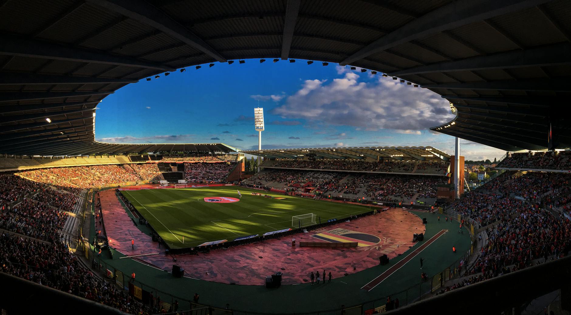 Aerial view of a bustling football stadium in Brussels, Belgium, filled with enthusiastic spectators under a blue sky.