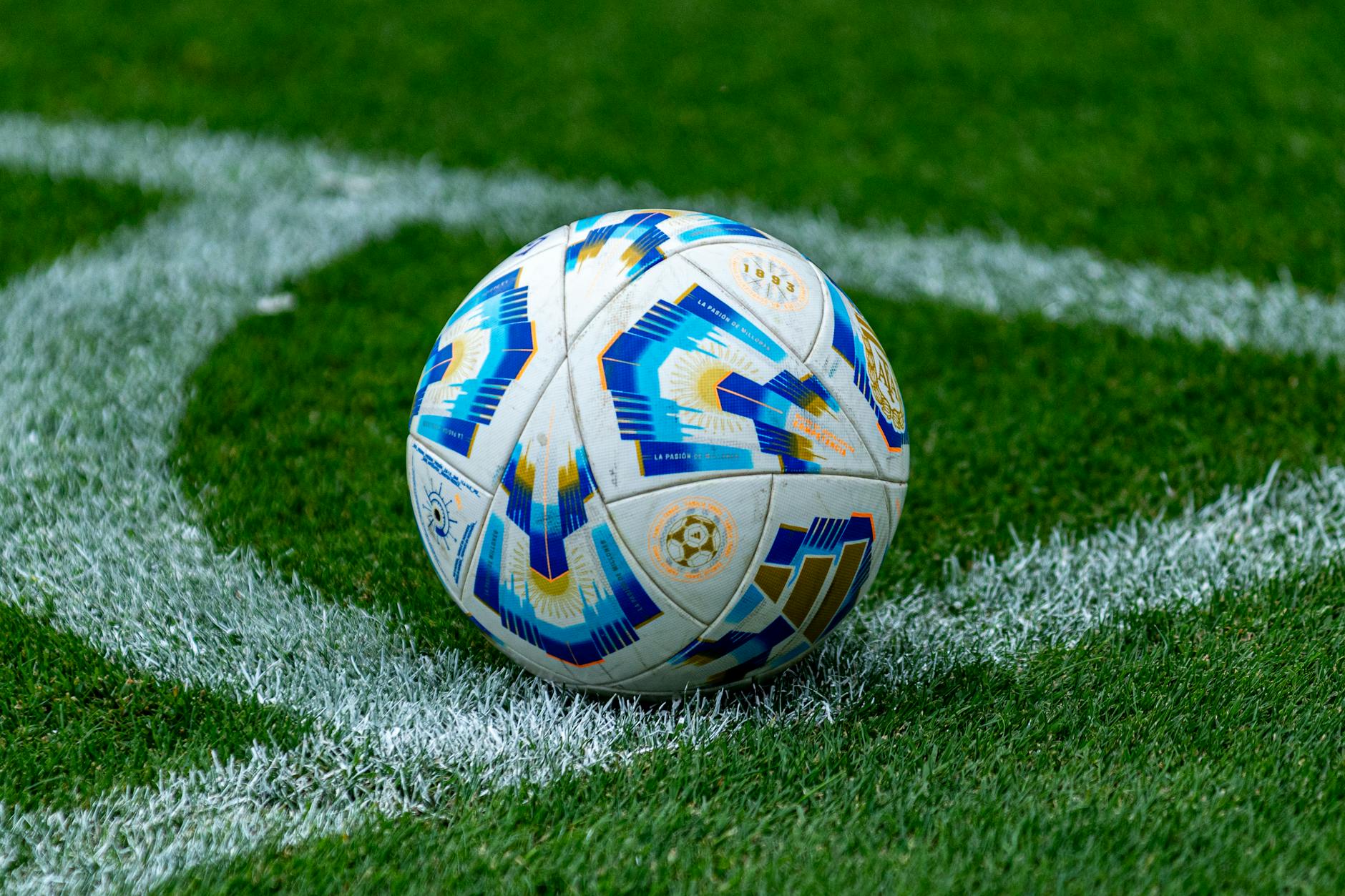 Colorful soccer ball resting on grassy corner field mark, symbolizing sports and competition.